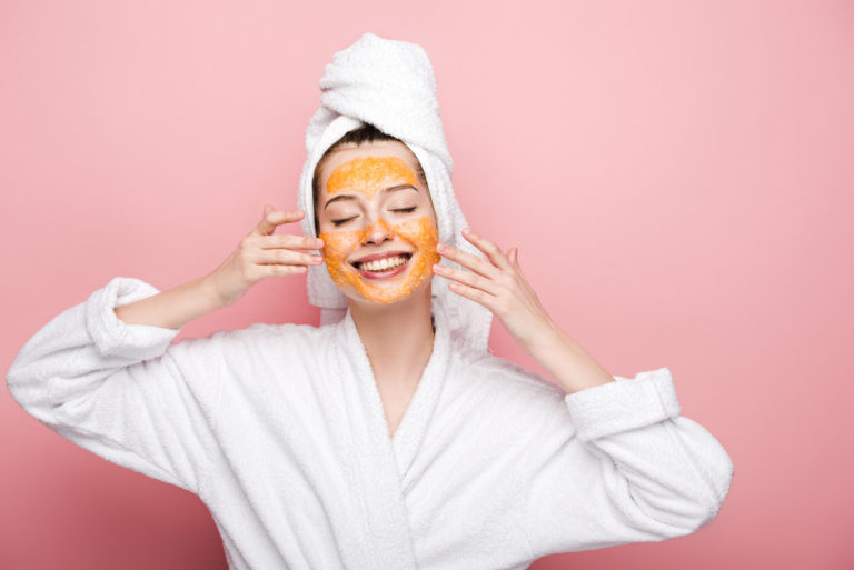 smiling girl with citrus facial mask touching face with closed e
